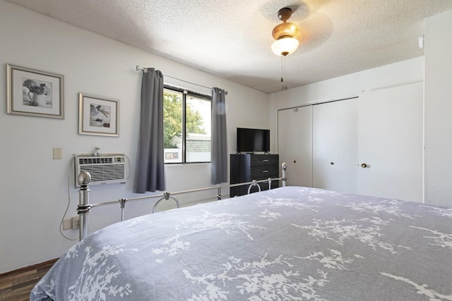 bedroom featuring dark hardwood / wood-style flooring, ceiling fan, a textured ceiling, a wall unit AC, and a closet