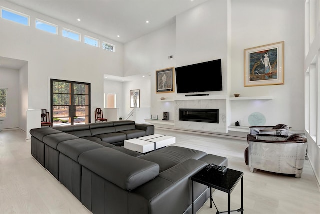 living room with a healthy amount of sunlight, a towering ceiling, a fireplace, and light wood-type flooring