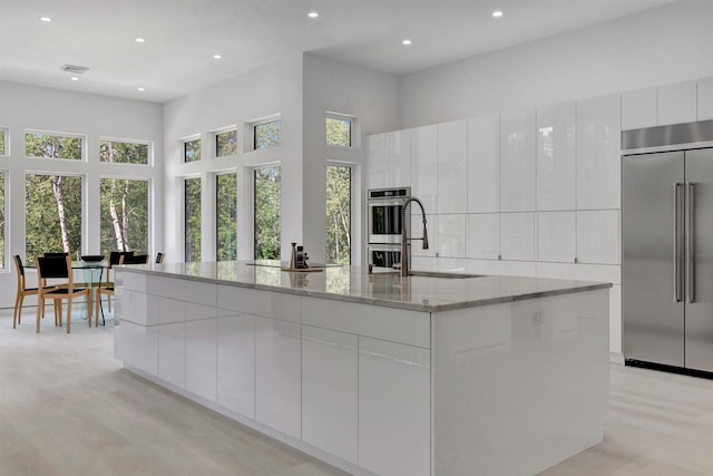 kitchen with stainless steel appliances, light stone countertops, a large island, and white cabinets