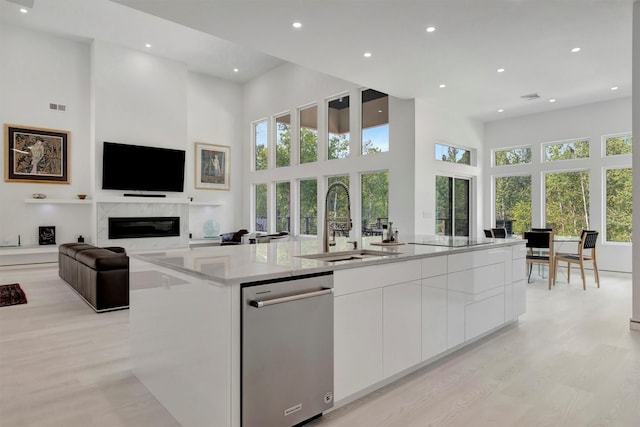 kitchen featuring sink, a kitchen island with sink, a towering ceiling, a high end fireplace, and white cabinets