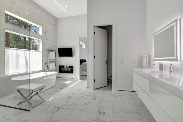 bathroom with a high ceiling, vanity, and a tub to relax in