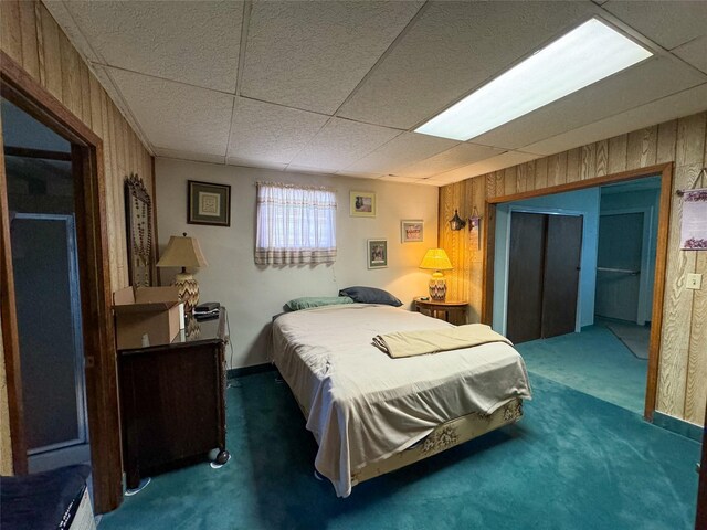 bedroom featuring dark colored carpet, a drop ceiling, and wood walls