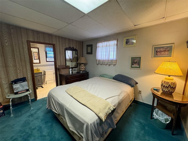 carpeted bedroom with connected bathroom, a paneled ceiling, and wood walls