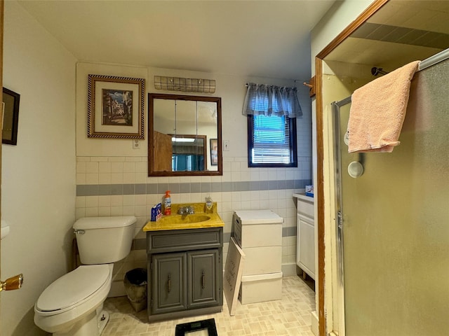 bathroom featuring vanity, toilet, a shower with door, and tile walls