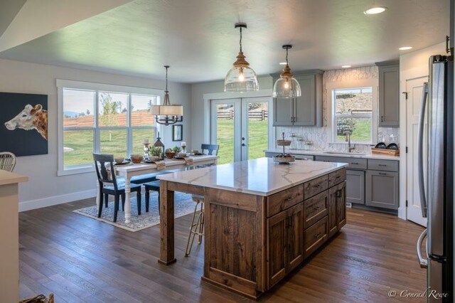 kitchen with a healthy amount of sunlight, tasteful backsplash, dark hardwood / wood-style flooring, pendant lighting, and stainless steel fridge