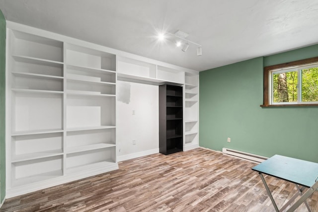 unfurnished bedroom featuring track lighting, baseboard heating, baseboards, and wood finished floors