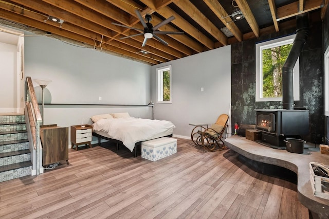 bedroom with a wood stove, multiple windows, wood finished floors, and baseboards