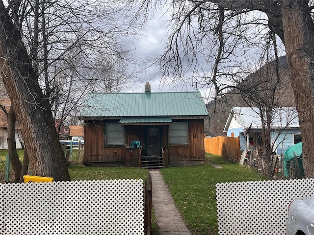 view of front of home with a chimney, metal roof, fence, a front lawn, and board and batten siding