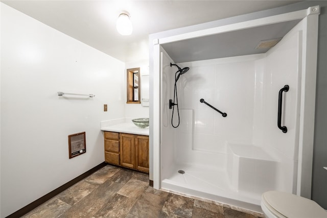 bathroom with toilet, a stall shower, vanity, stone finish flooring, and baseboards