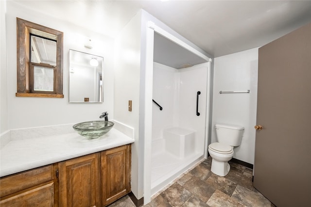 bathroom featuring toilet, baseboards, stone finish floor, a shower stall, and vanity