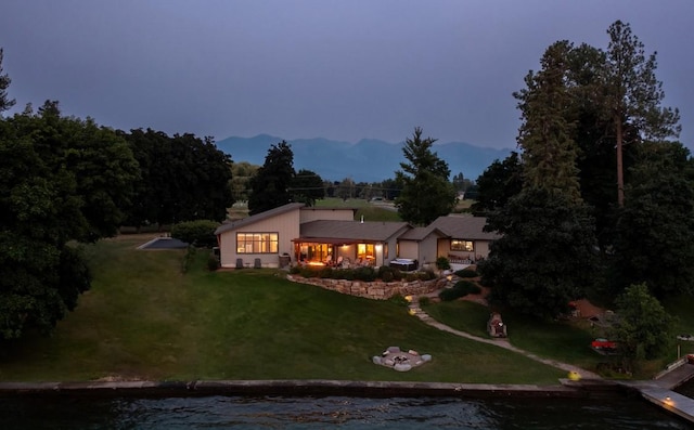 back house at dusk featuring a water view and a lawn