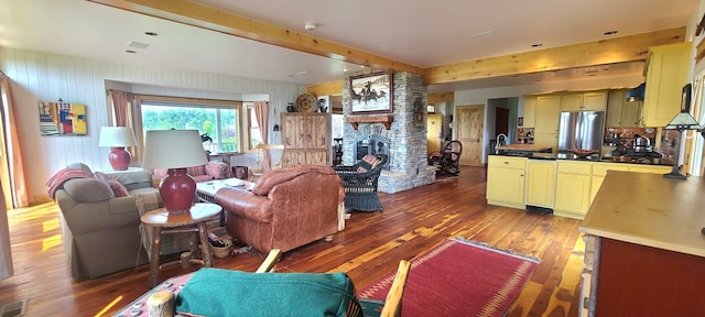 living room featuring wooden walls, dark hardwood / wood-style floors, beamed ceiling, and a stone fireplace