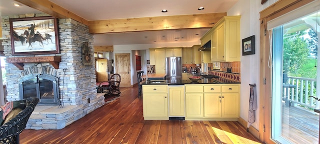 kitchen with cream cabinets, a fireplace, stainless steel fridge, dark hardwood / wood-style floors, and tasteful backsplash