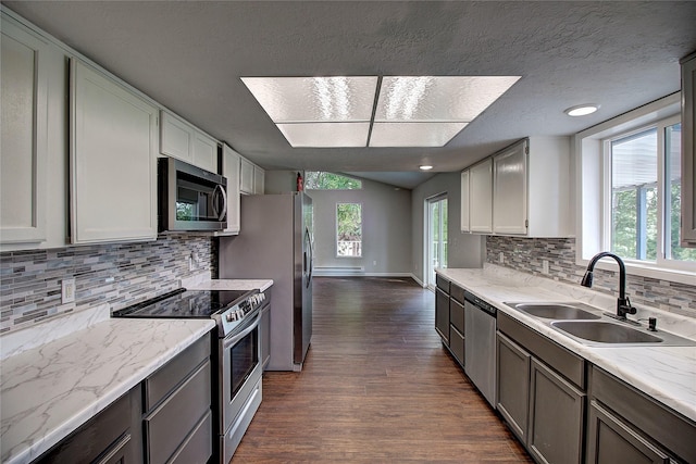 kitchen featuring stainless steel appliances, dark wood-type flooring, vaulted ceiling, a sink, and light stone countertops