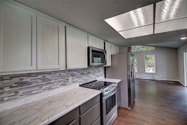 kitchen with dark wood-type flooring, light stone countertops, stainless steel appliances, a baseboard heating unit, and backsplash