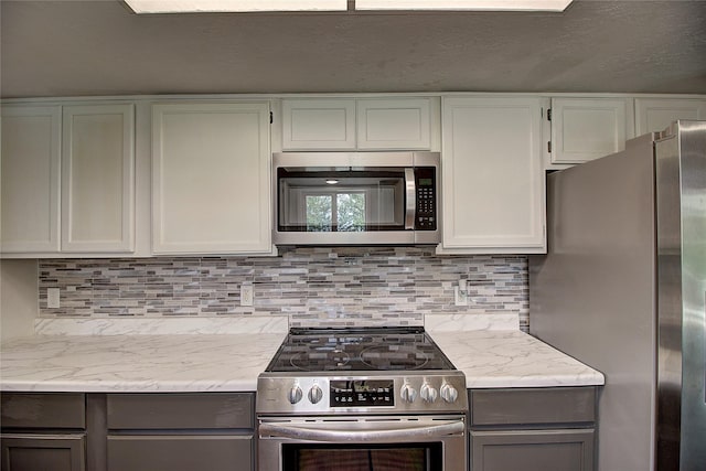 kitchen featuring stainless steel appliances, gray cabinets, light stone countertops, and decorative backsplash