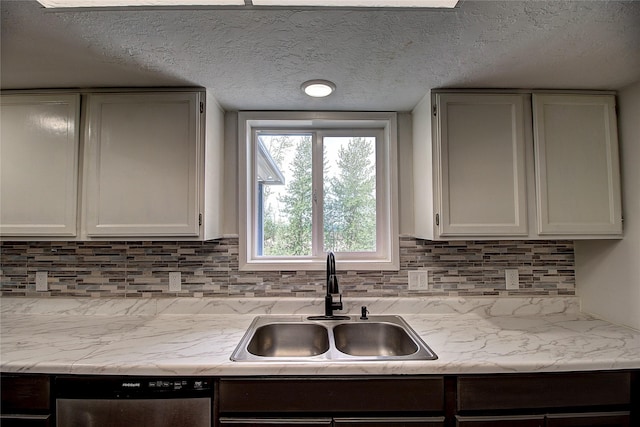 kitchen featuring a textured ceiling, a sink, light countertops, decorative backsplash, and dishwasher