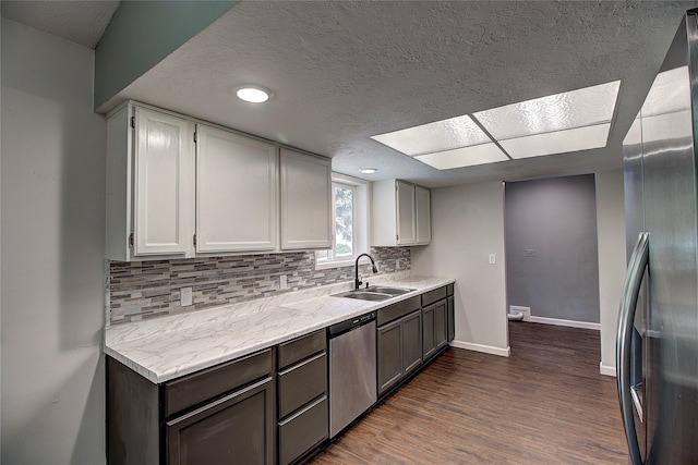 kitchen with stainless steel appliances, dark wood-type flooring, a sink, baseboards, and tasteful backsplash