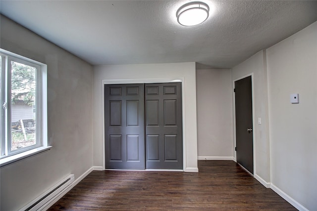 unfurnished bedroom featuring a baseboard radiator, a closet, multiple windows, and dark wood finished floors