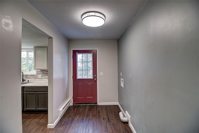 doorway to outside with a baseboard heating unit, a textured ceiling, dark wood finished floors, and baseboards