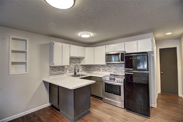 kitchen featuring light countertops, appliances with stainless steel finishes, a sink, wood finished floors, and a peninsula