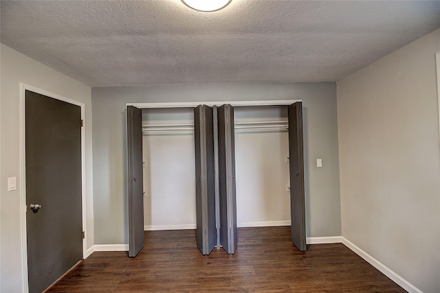 unfurnished bedroom featuring dark wood-style floors, a closet, a textured ceiling, and baseboards