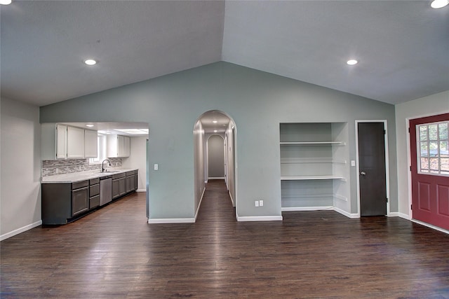 unfurnished living room with arched walkways, lofted ceiling, a sink, baseboards, and dark wood-style floors