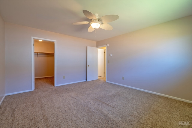 unfurnished bedroom with a walk in closet, light colored carpet, a closet, and ceiling fan