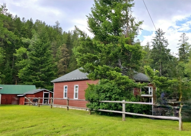 rear view of property featuring a lawn, an outdoor structure, and fence