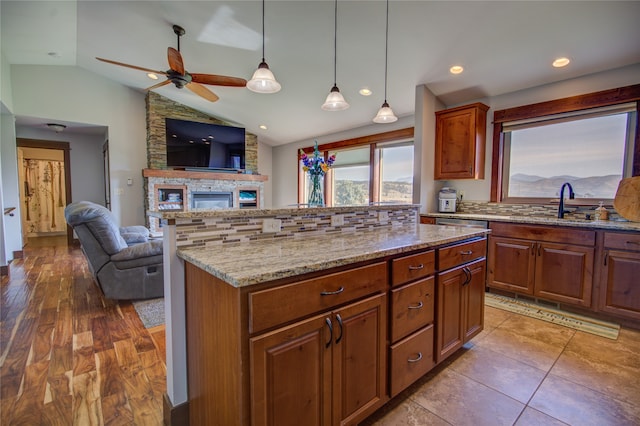 kitchen with vaulted ceiling, ceiling fan, a kitchen island, and a stone fireplace