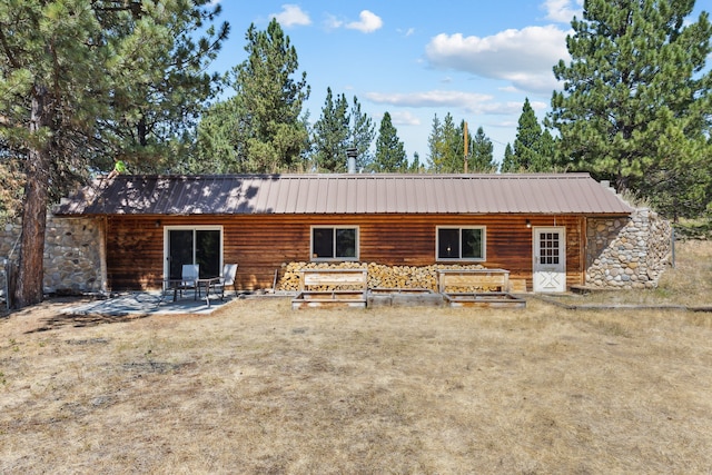 rear view of property with metal roof, a patio area, and stone siding