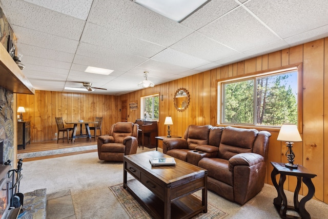 carpeted living area featuring a drop ceiling, ceiling fan, and wood walls