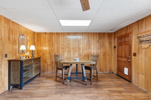 dining area with wooden walls, wood finished floors, and a paneled ceiling