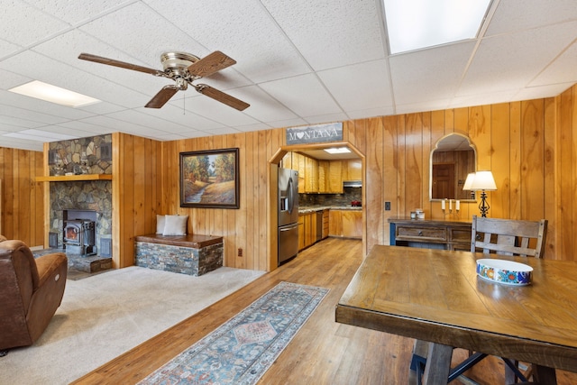 interior space featuring a wood stove, wooden walls, a paneled ceiling, light wood-type flooring, and a ceiling fan