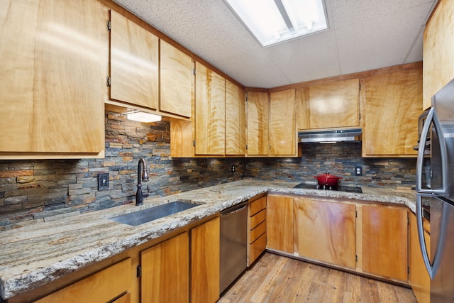 kitchen with appliances with stainless steel finishes, light wood-style flooring, light stone countertops, a sink, and under cabinet range hood