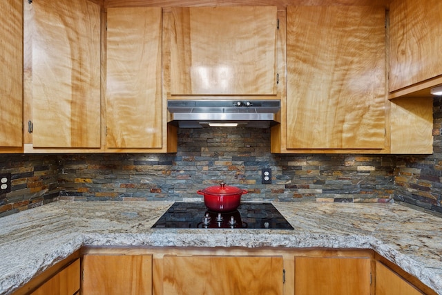 kitchen featuring tasteful backsplash, brown cabinets, black electric cooktop, light stone counters, and under cabinet range hood