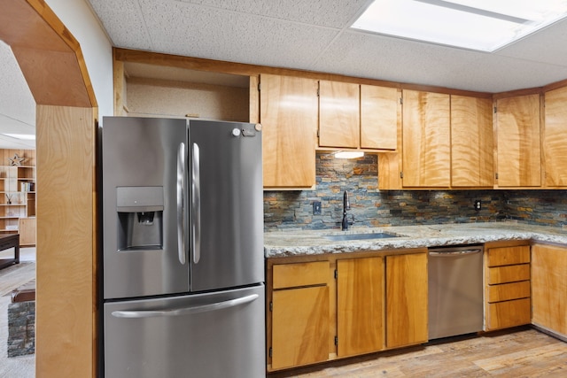 kitchen featuring a sink, light wood-style flooring, light stone counters, appliances with stainless steel finishes, and tasteful backsplash