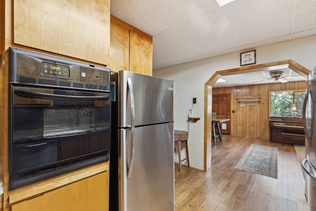 kitchen featuring freestanding refrigerator, a drop ceiling, dobule oven black, arched walkways, and wood finished floors