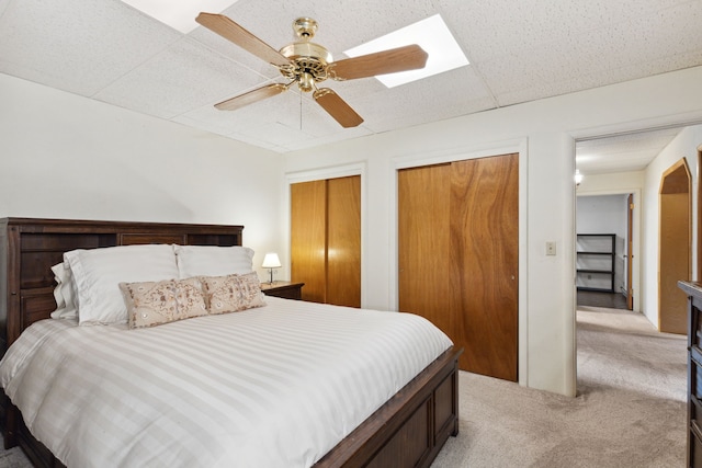 bedroom with light colored carpet, a ceiling fan, two closets, and a drop ceiling