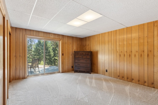 carpeted spare room with wooden walls and a paneled ceiling