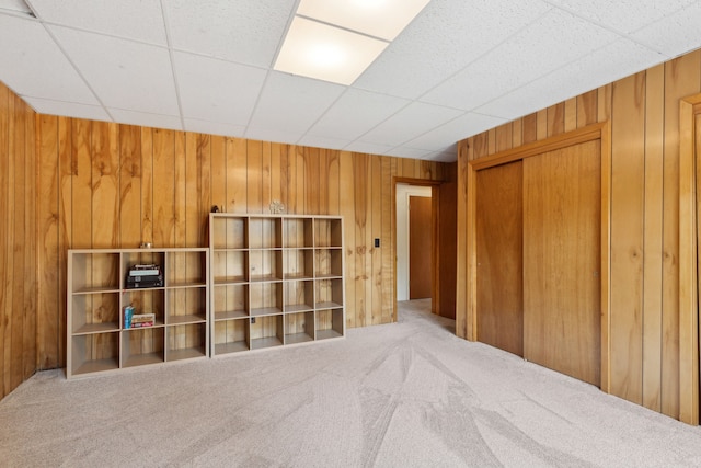 unfurnished room with wooden walls, a drop ceiling, and light carpet