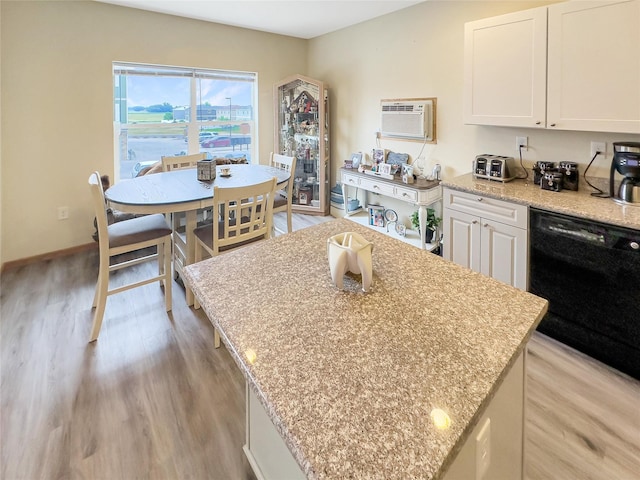 kitchen featuring a kitchen island, white cabinetry, black dishwasher, light stone counters, and light hardwood / wood-style flooring