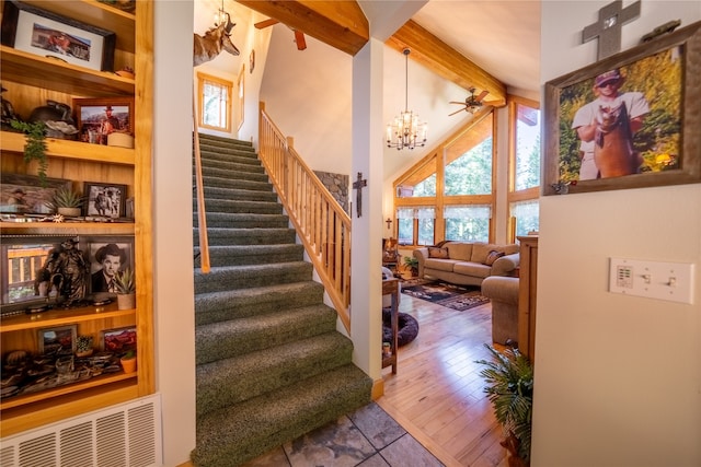 stairs with beamed ceiling, ceiling fan with notable chandelier, hardwood / wood-style flooring, and high vaulted ceiling