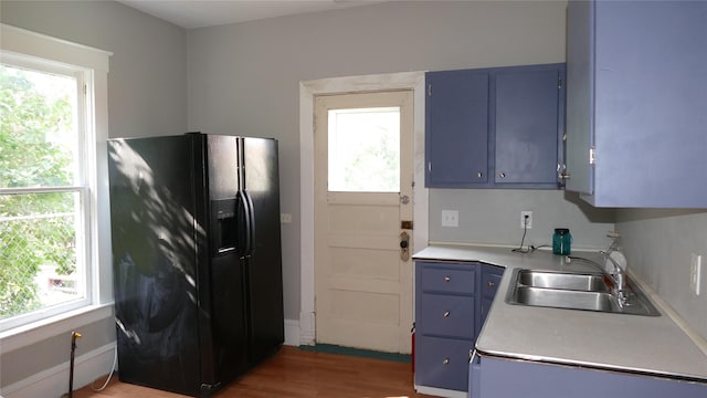 kitchen featuring blue cabinetry, dark hardwood / wood-style floors, black fridge with ice dispenser, and sink