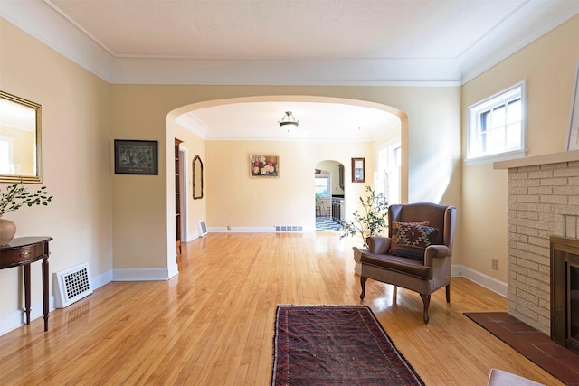 living area with a brick fireplace, crown molding, and light hardwood / wood-style floors