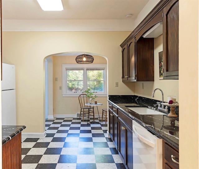 kitchen featuring white appliances, dark brown cabinetry, sink, and dark stone countertops