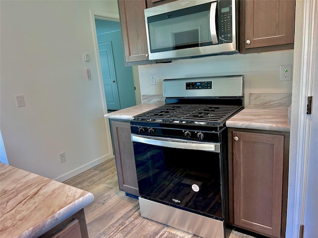 kitchen with dark brown cabinetry, stainless steel appliances, and light hardwood / wood-style floors