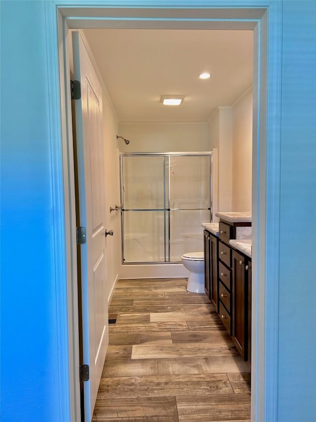 bathroom with crown molding, vanity, wood-type flooring, a shower with shower door, and toilet