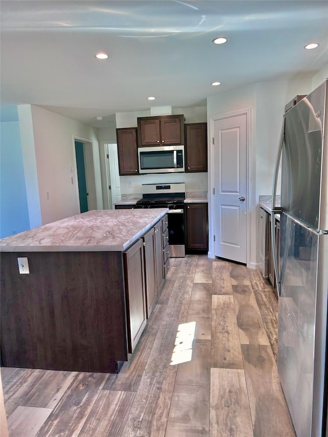 kitchen with appliances with stainless steel finishes, a center island, dark brown cabinetry, and light hardwood / wood-style floors