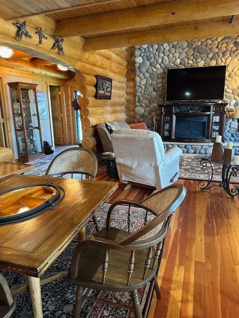 dining space featuring hardwood / wood-style flooring, wooden ceiling, beamed ceiling, a stone fireplace, and log walls